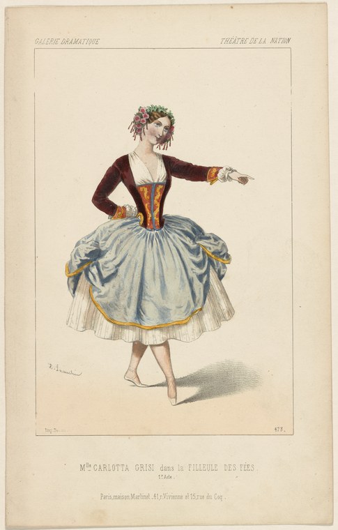 A female dancer in a brown velvet jacket and pale blue skirt with orange trim, extending her left arm in gesture, standing en demi-pointe.
