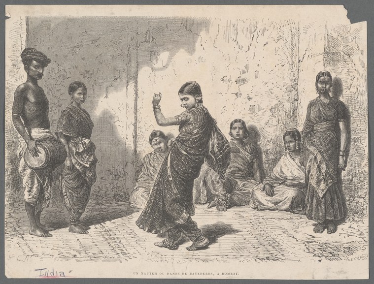 Woman in ornate sari and jewelry stands with raised arm amid gathered crowd in narrow alleyway, watched intently by seated and standing onlookers.