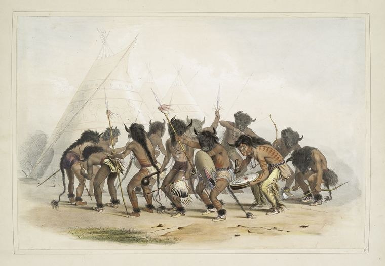 Group of Indigenous male dancers in circle formation before a tipi, wearing ornaments and headdresses, bodies in mid-leap and extended movement with raised