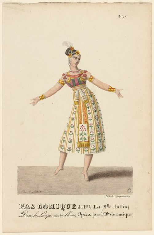 A woman in an ornate tunic and patterned skirt with a feathered headdress stands barefoot with arms extended, in a theatrical pose.