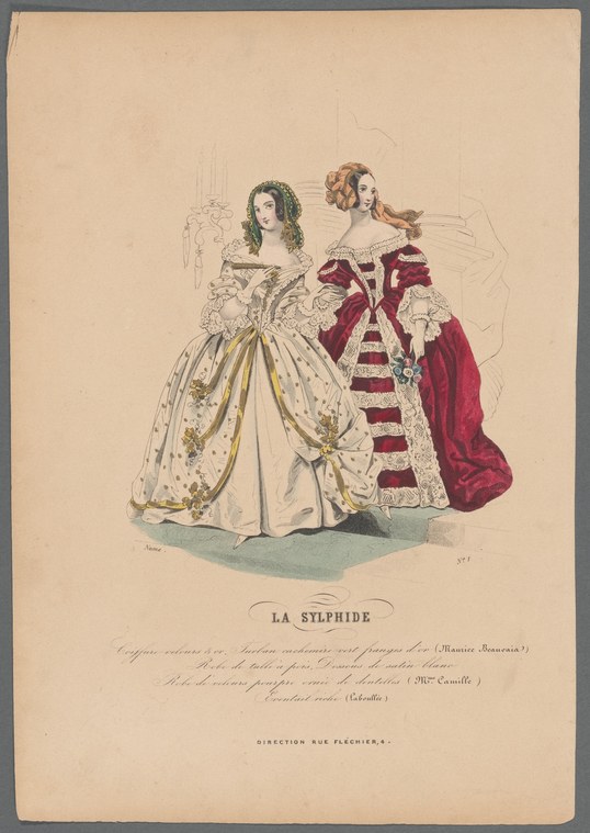 Two women in elaborate stage costumes stand side by side: one in a pale embroidered gown with off-shoulder neckline, the other in crimson velvet with white fur