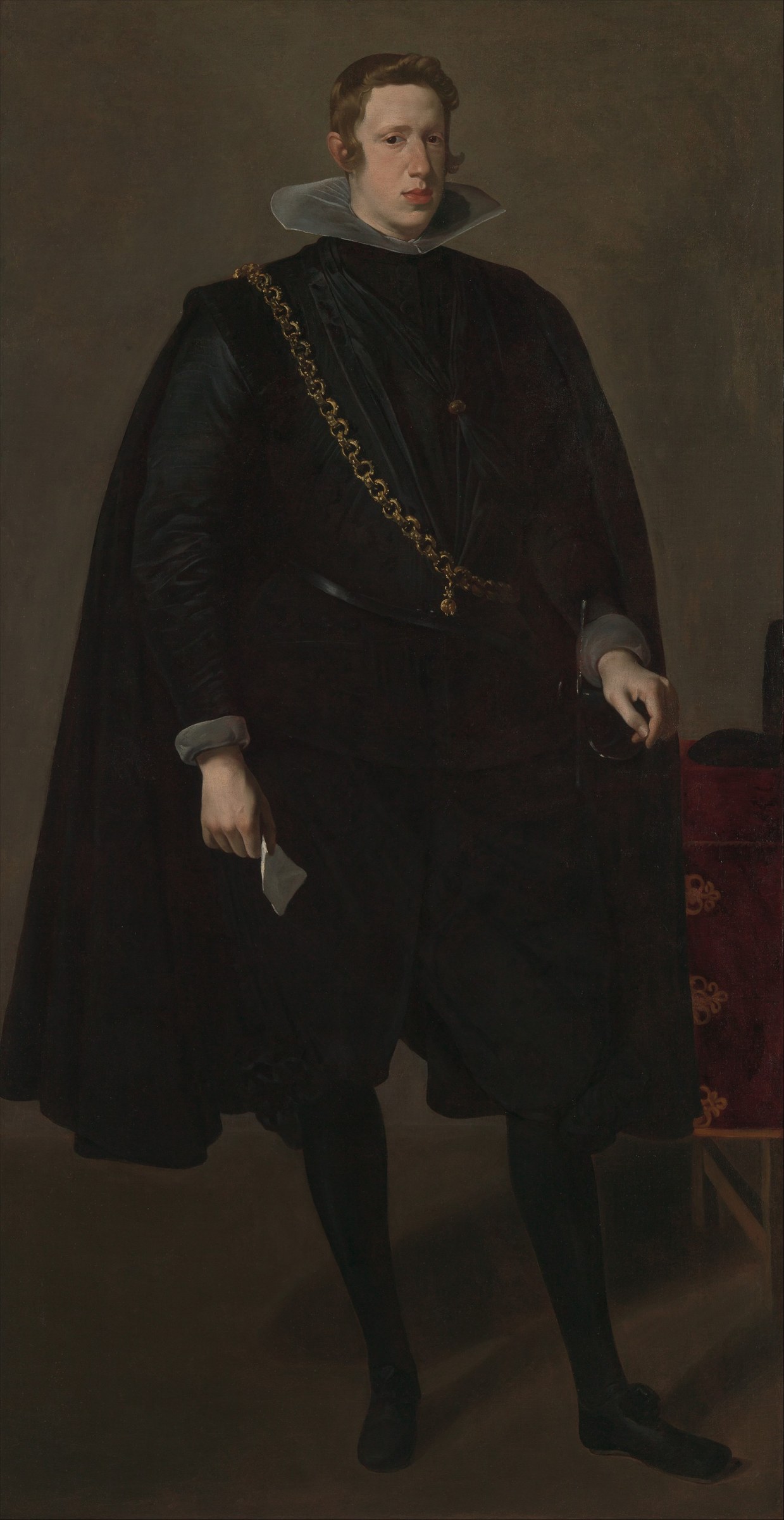 Portrait of a young man in black velvet cape and doublet, standing upright against a neutral ground, holding a folded paper.