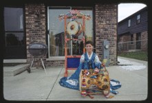 Korean dancer in blue dress standing posed in front of traditional East Asian building with ornate roof, 1977