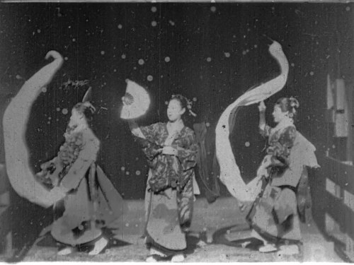 Three female dancers in flowing Japanese costumes pose against a dark starry backdrop, two with arms raised in curved gestures.