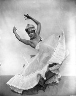 Solo dancer in mid-leap, arms extended, gauzy skirt billowing, against plain background.