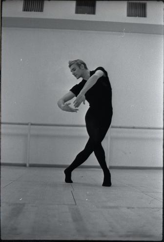 Male ballet dancer in black leotard twists torso with asymmetrical arm position in white studio, 1968 photograph.