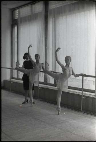 Three ballet dancers in a studio, each performing an arabesque at the barre under natural light.