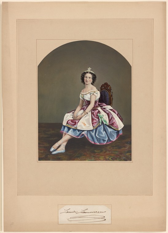 A young ballerina in a pale tulle tutu and tiara sits on a wooden stage floor, one leg extended, in an informal pose.