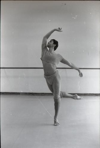 Male ballet dancer in a studio, standing on one leg with the other extended, arm raised above his head in classical arabesque pose.
