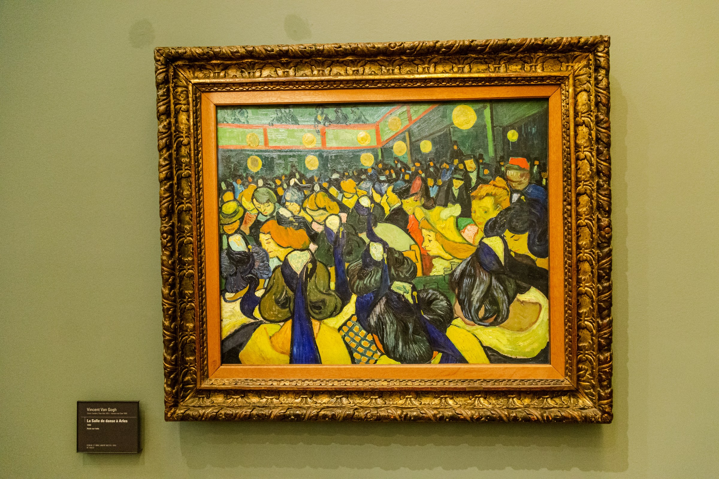 Densely packed figures in yellows and blues dance in a crowded interior lit by hanging lamps.