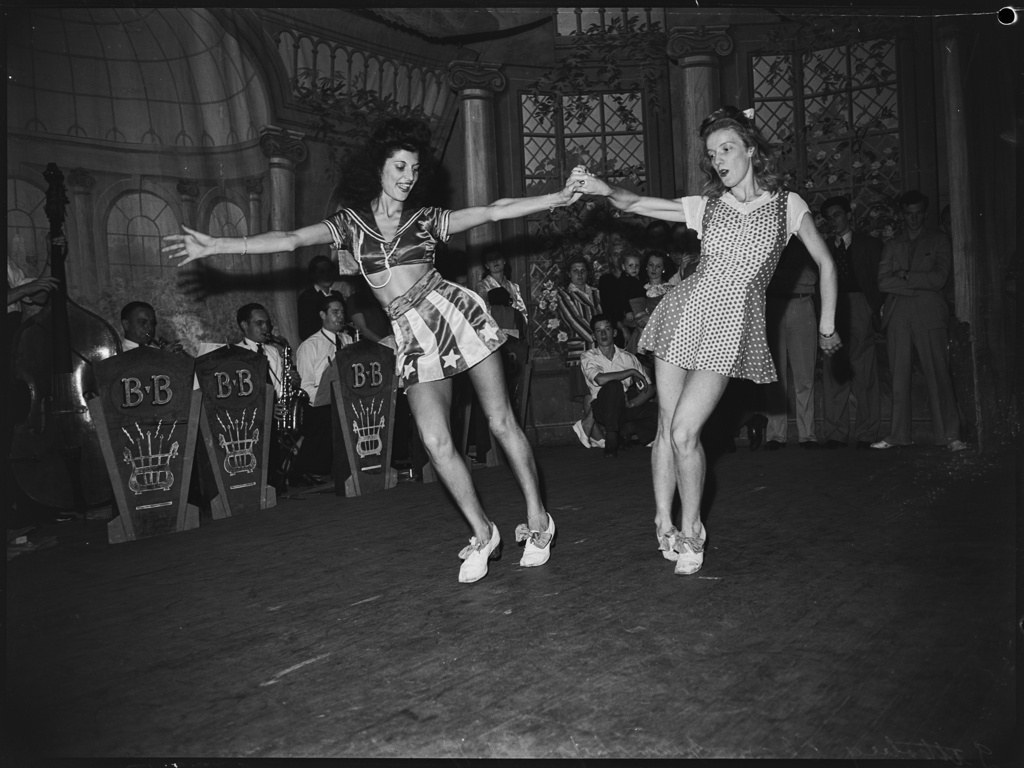 Two couples in 1940s dress jitterbug energetically on a crowded ballroom floor at the Trocadero, Sydney, watched by formally dressed spectators