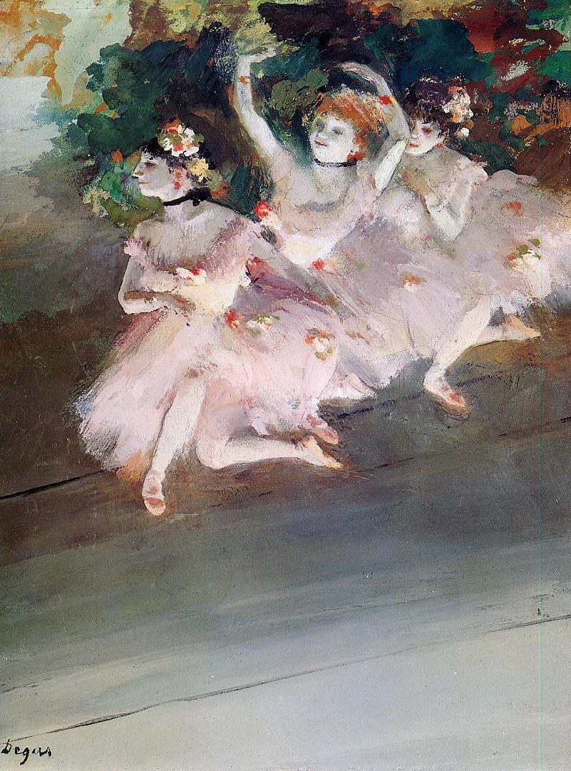 Three young women in pink tutus and flowers sit on a gray stage floor surrounded by dense dark foliage.