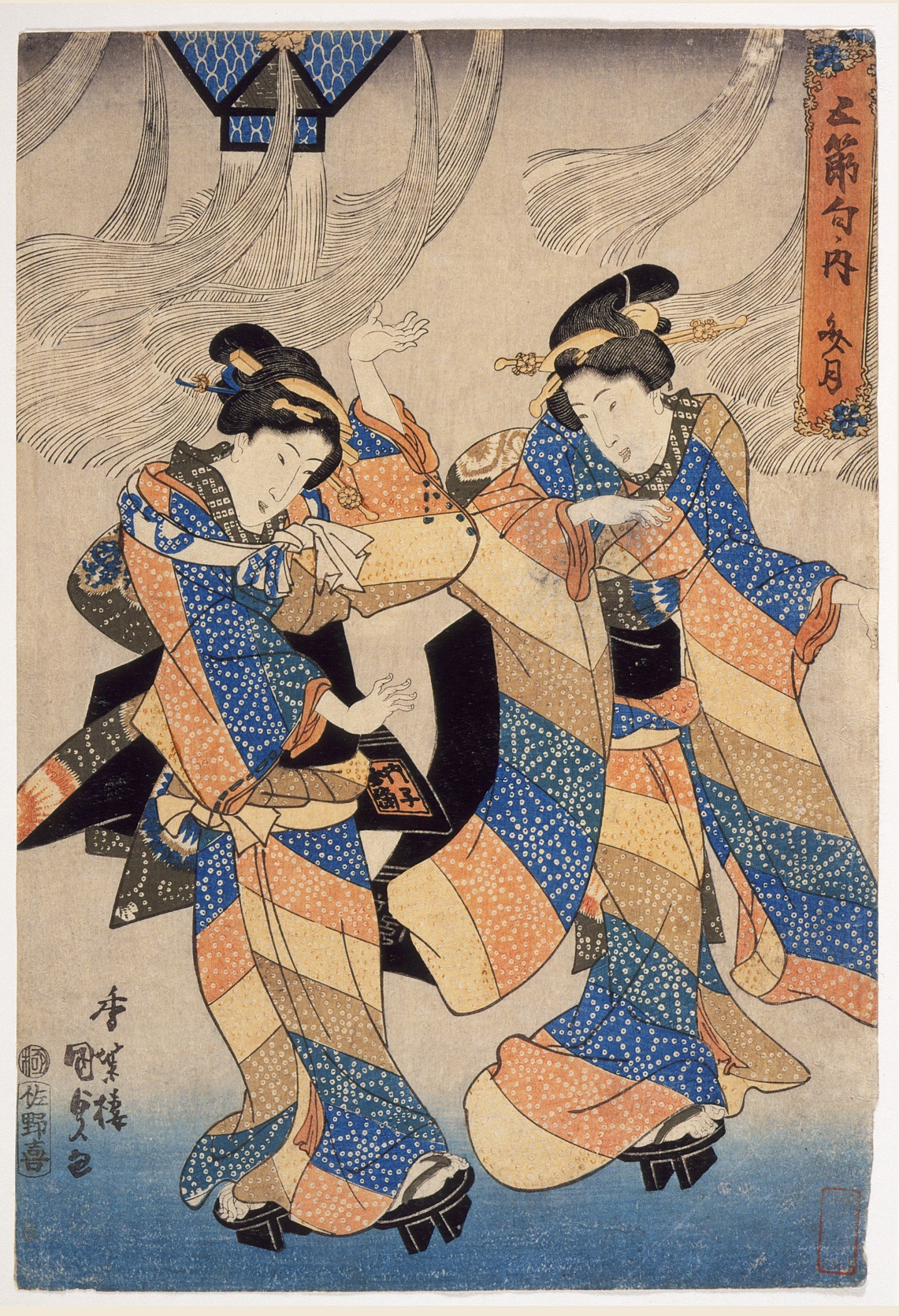 Two women in layered blue and orange robes dance in synchronized movement, their arms extended and mirrored, indoors beneath a blue canopy.