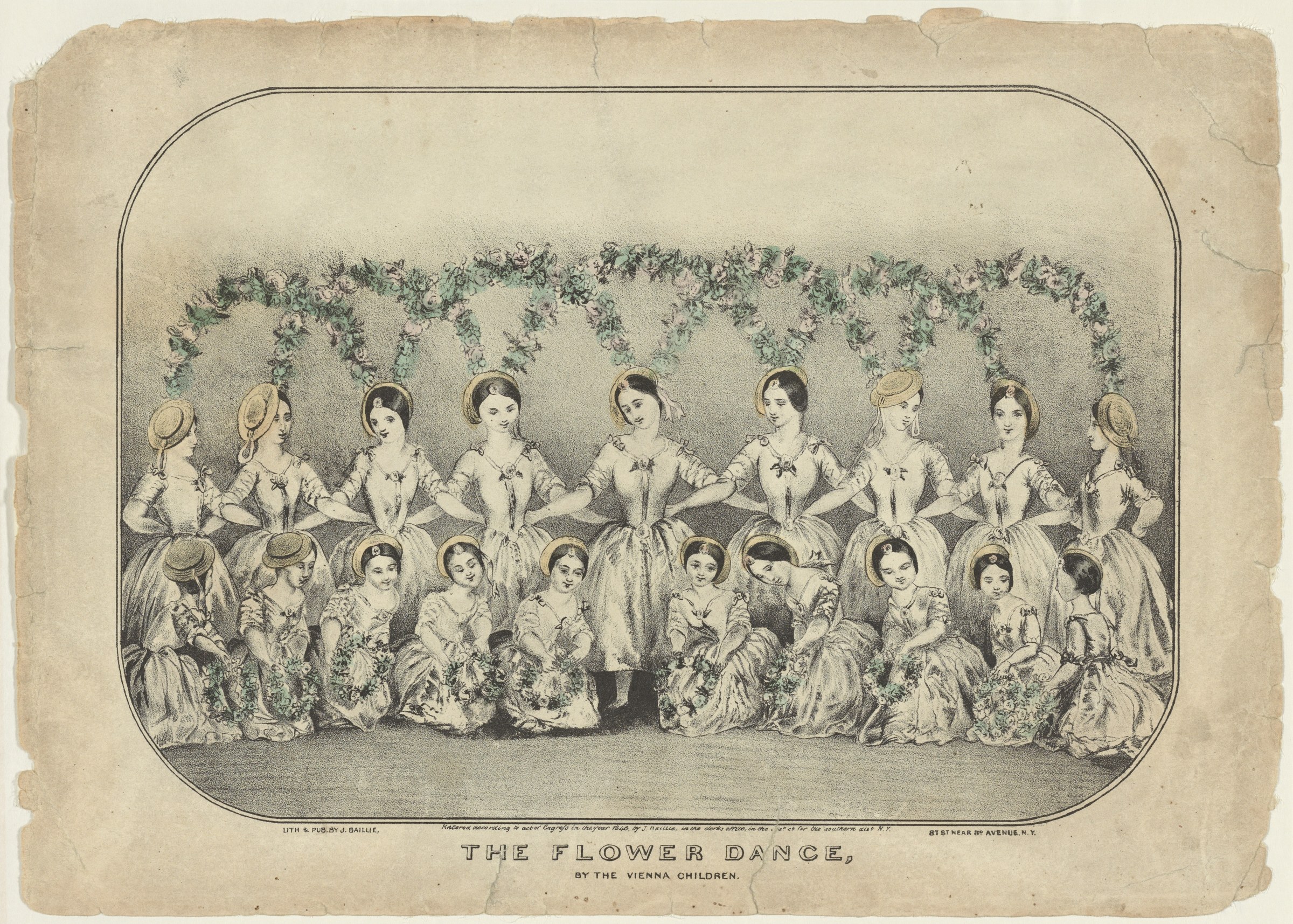 Twenty young female dancers in white dresses with bonnets stand and kneel in two rows against a floral garland, posed formally without moving or touching.