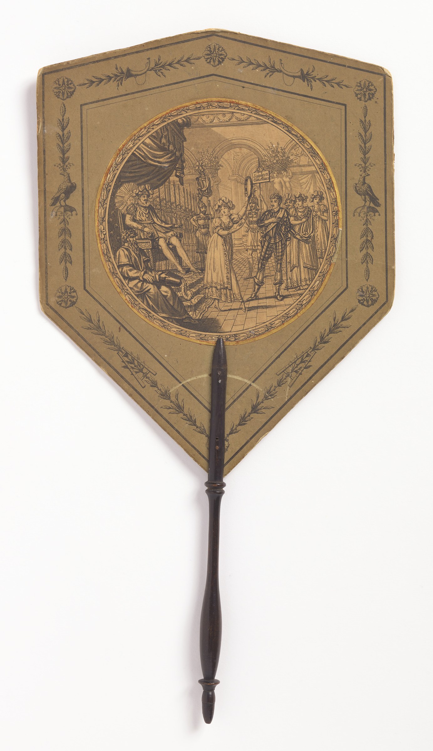Shield-shaped hand screen with engraved scene of woman playing tambourine before a seated king and assembled courtiers in a classical palace setting.