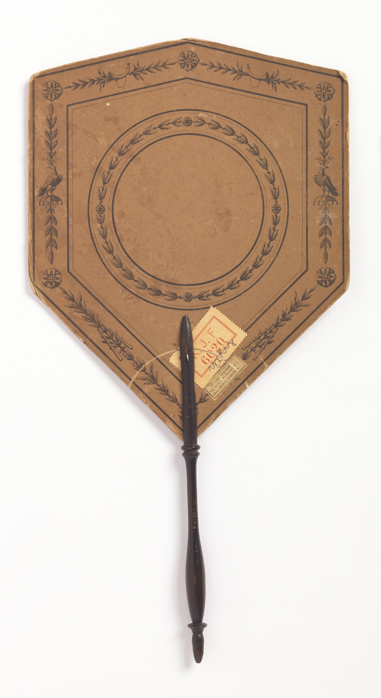 Shield-shaped decorative fan with engraved borders showing a classical female dancer playing tambourine before two uniformed men.