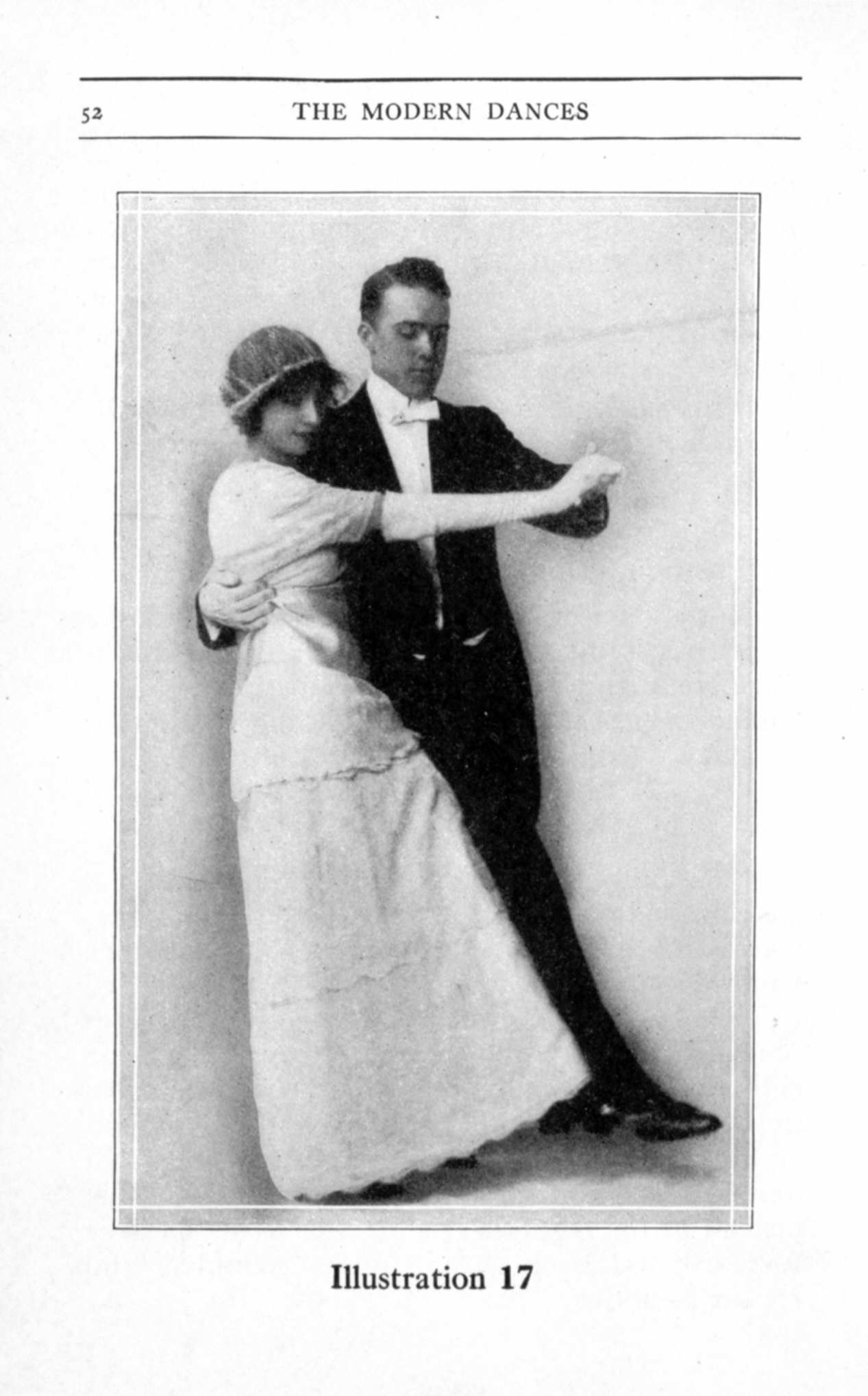 A man in tailcoat and a woman in a long white gown with cloche hat stand in closed ballroom hold, posed for a dance instruction photograph.