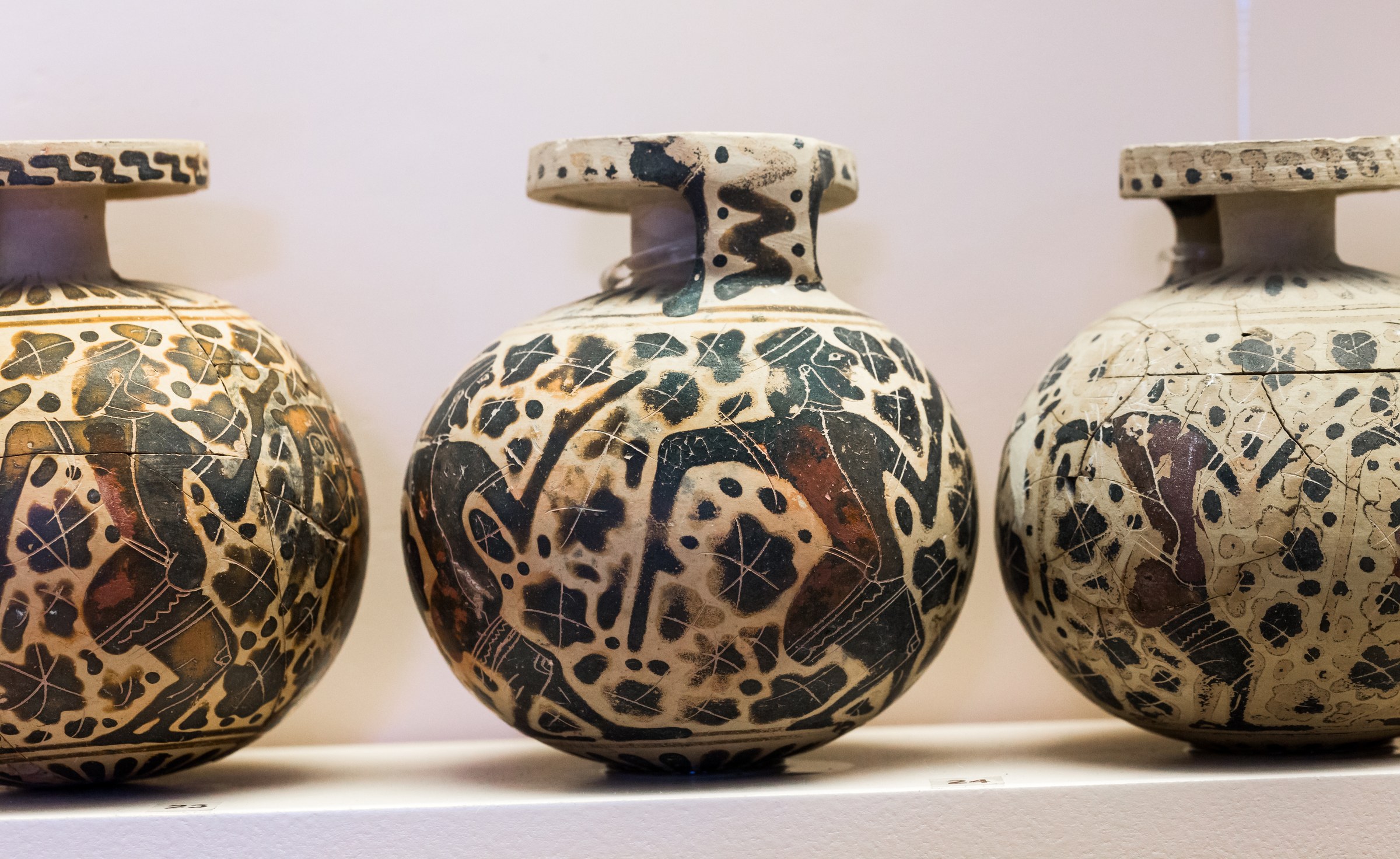 Three small cream and black decorated ceramic vessels with bulging bodies and loop handles, covered in figures of padded performers.