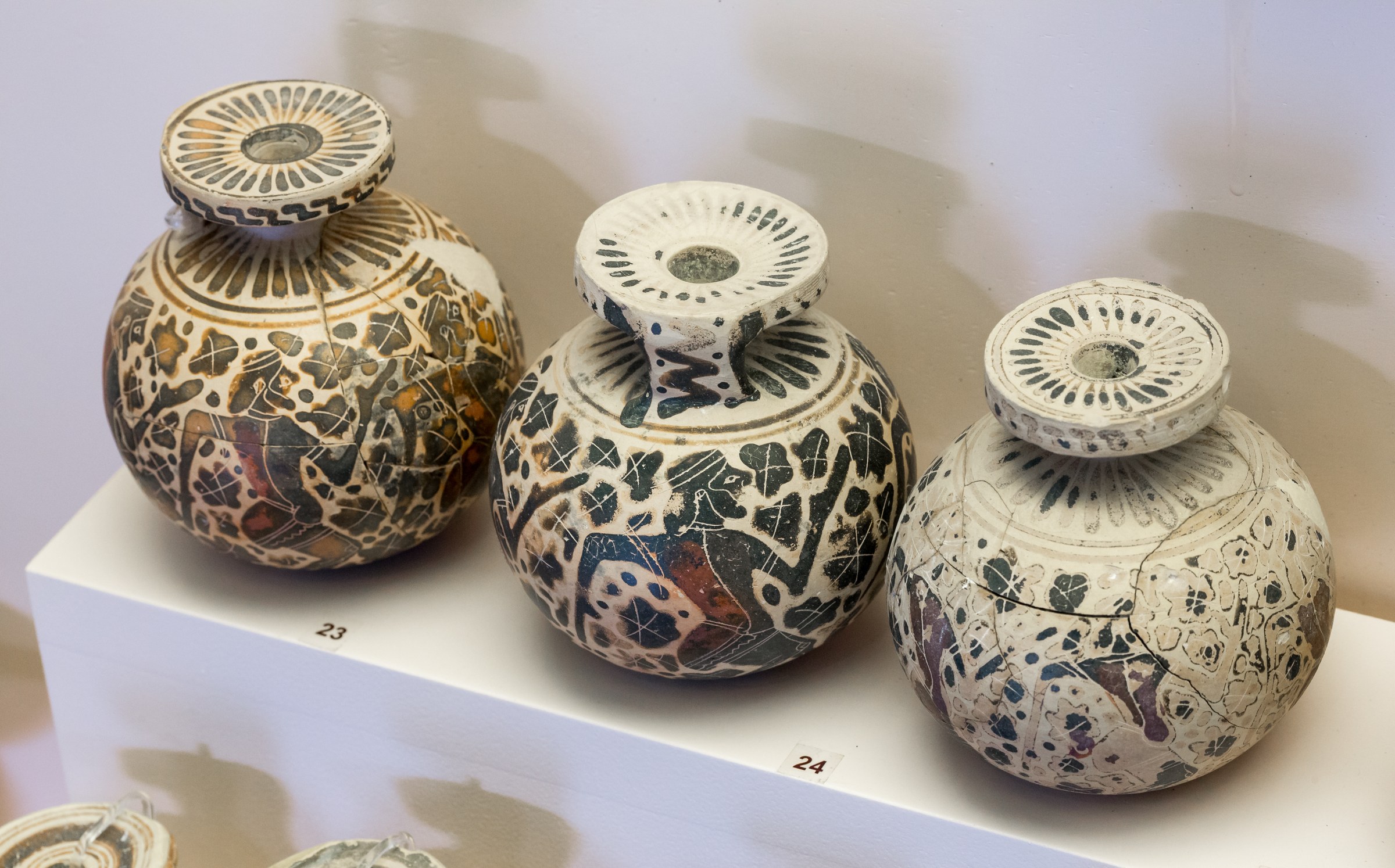 Three ancient Corinthian pottery vessels decorated with repeated silhouettes of padded male dancers in black-figure technique.