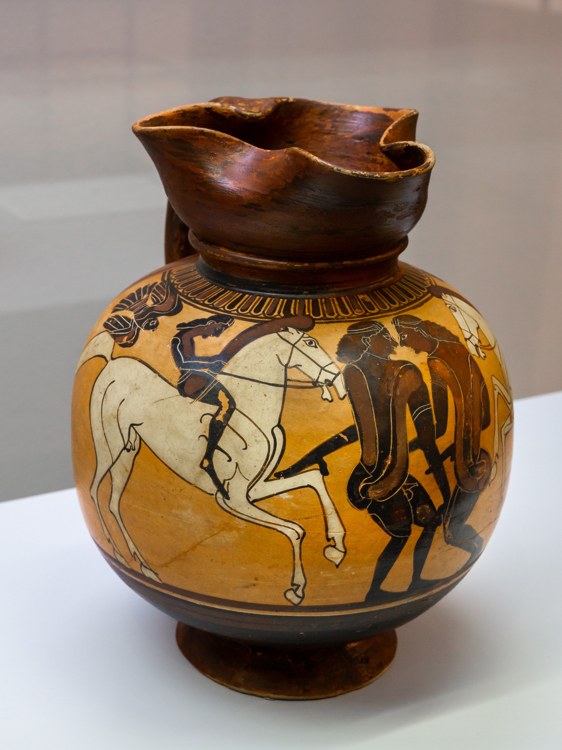 Ancient Greek ceramic jug with two padded male dancers facing each other, flanked by horsemen and eagles, rendered in black-figure technique.