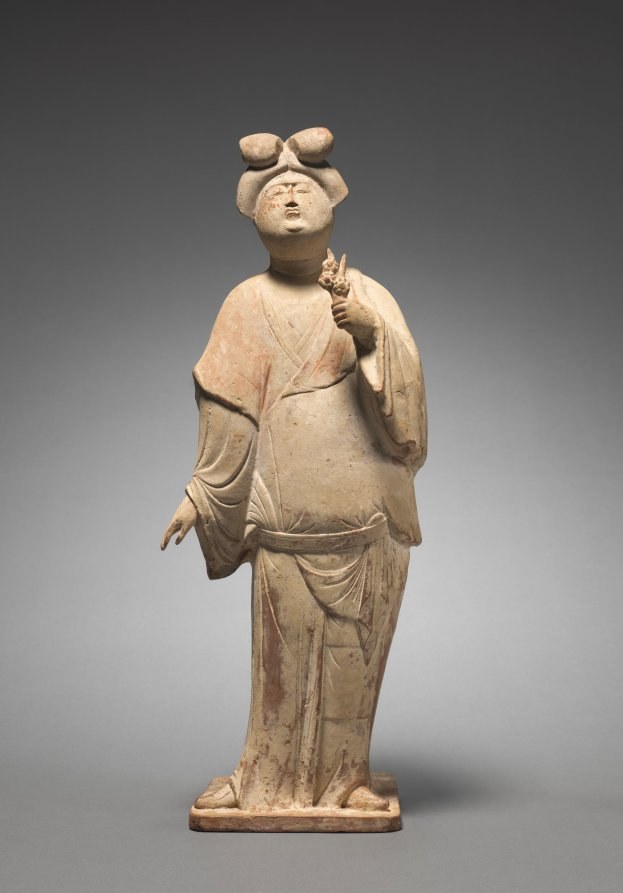 Terracotta figurine of a Tang dynasty woman in layered robes, hands folded, standing with upturned hairstyle and ornaments.