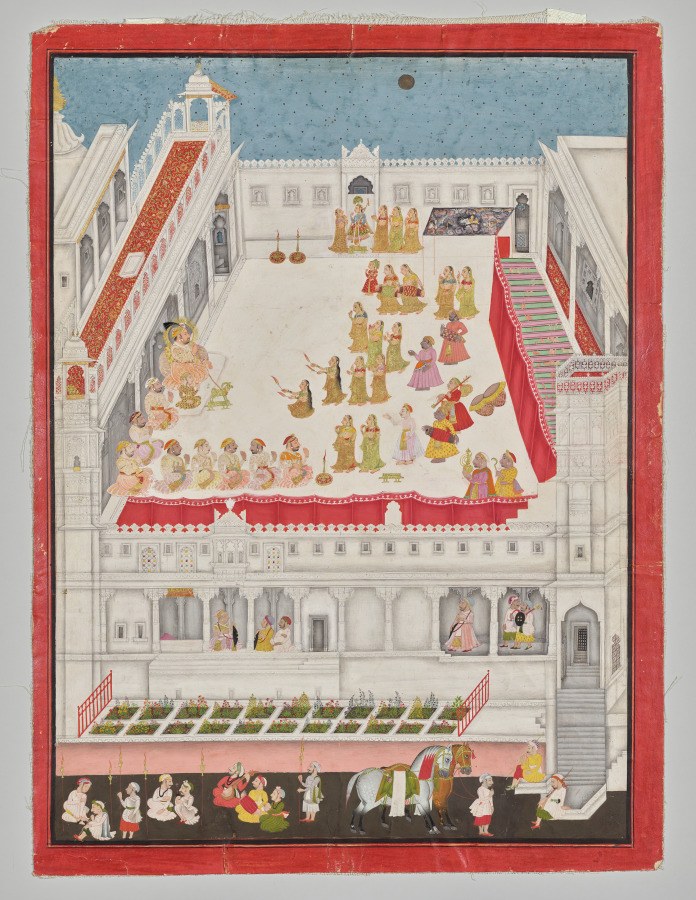 Palace courtyard at night with dozens of costumed dancers, musicians, and courtiers surrounding a figure in blue with a peacock-feather crown, watched by the