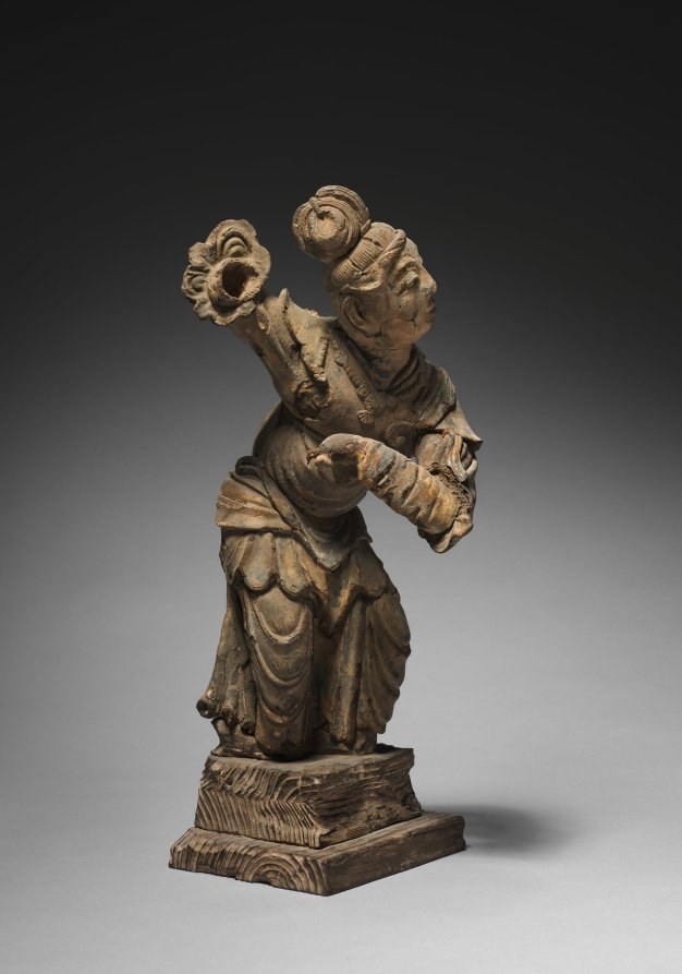 Wooden sculpture of a celestial dancer with arched spine, raised arms holding flowers, flowing robes, tilted head.