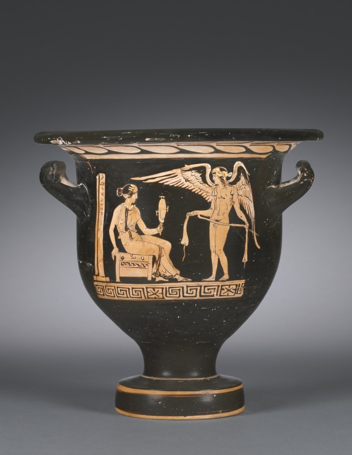 A seated woman gazes into a mirror while winged Eros stands nearby holding a ribbon, on a black-glazed Greek pottery vessel.