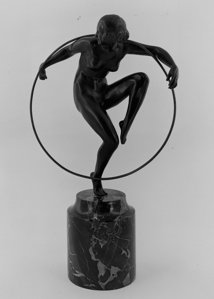 Bronze sculpture of a female acrobat balanced on one leg, gripping a large hoop with both hands, body arched forward in dynamic tension.