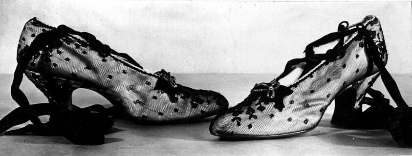 Pair of ornate women's heeled dance shoes with lace uppers, rhinestone and metal buckle embellishments, and trailing silk ribbon ties.