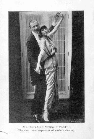 A man in a dark tailcoat supports a woman in a light ballroom gown in a dramatic lifted position, her body arched and arm extended upward, against a plain