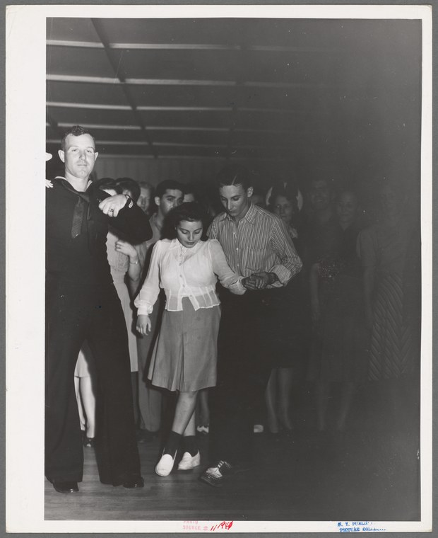 Black and white photograph of a young couple dancing close together in a crowded ballroom, 1940s, identified as newlyweds at Sherman's dance hall.