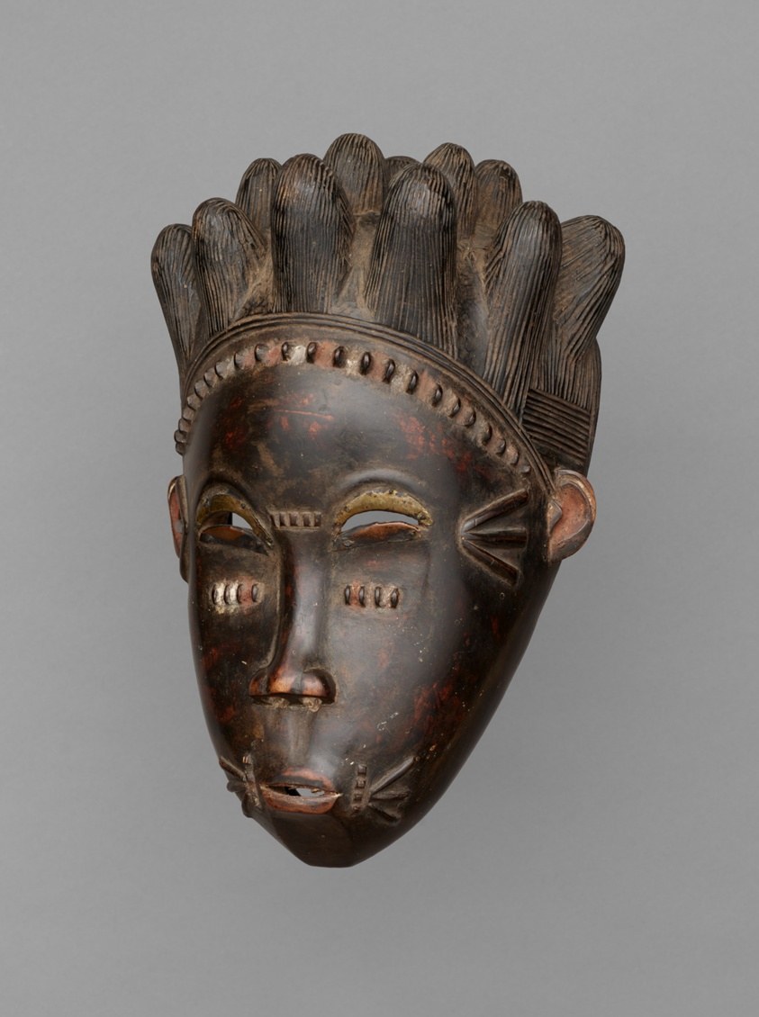 Wooden face mask with tall fan-shaped headdress, copper-inlaid eyes, traces of red pigment, carved by Baule artisans.