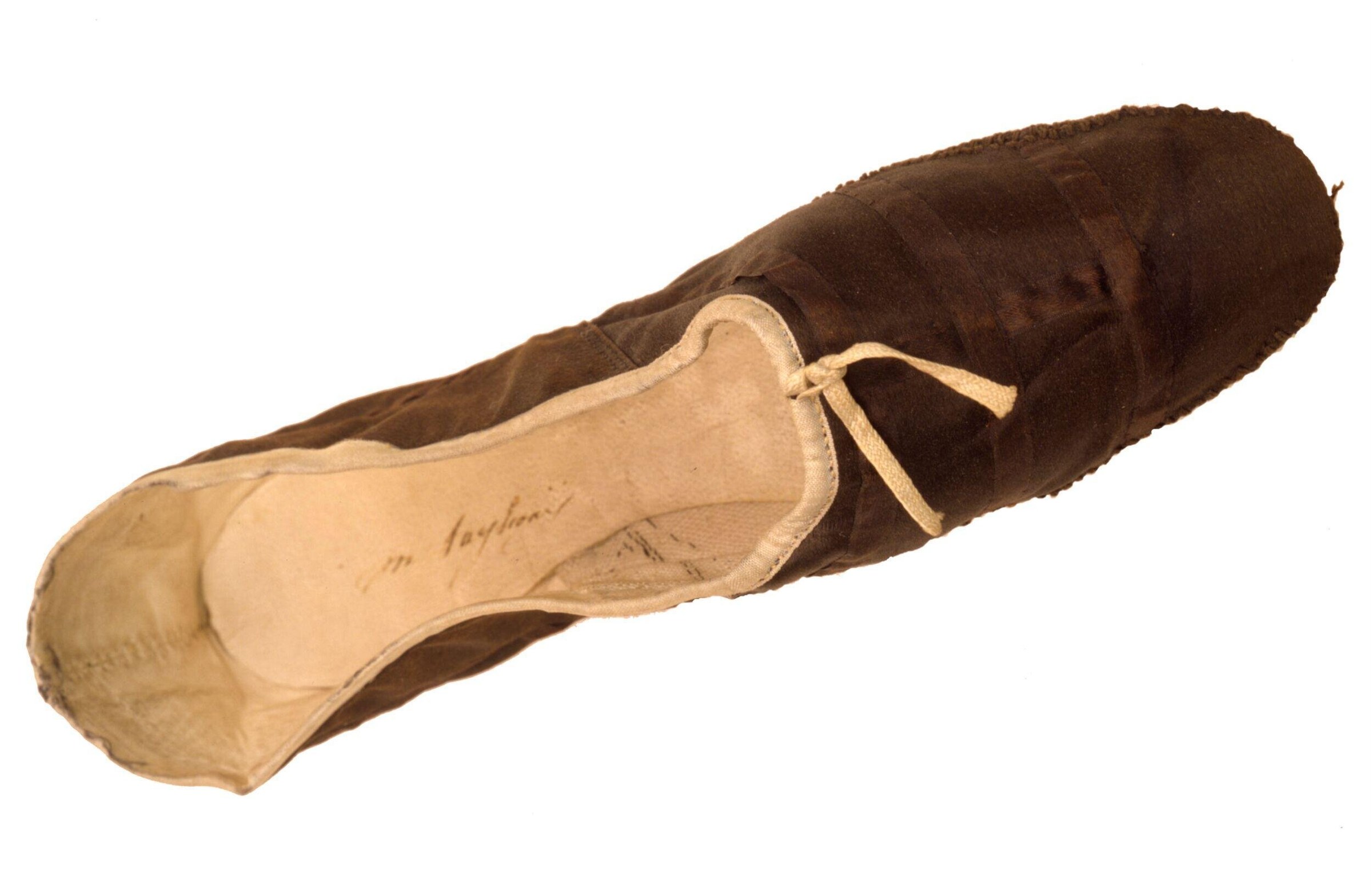 A worn ballet pointe shoe with pale satin vamp and dark brown heel cuff, photographed against white background.