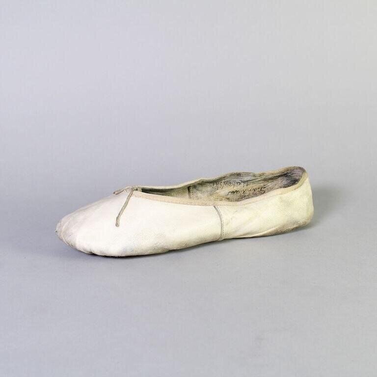 A worn pink satin ballet pointe shoe, sole darkened with use, against a gray background.