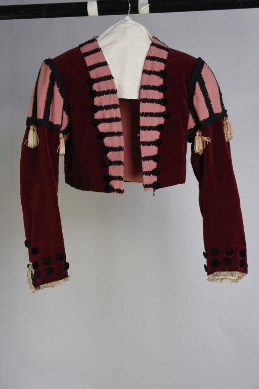 Burgundy velvet bolero jacket with striped facing, button-trimmed cuffs, and cream silk tassels at the shoulders, displayed on a hanger.