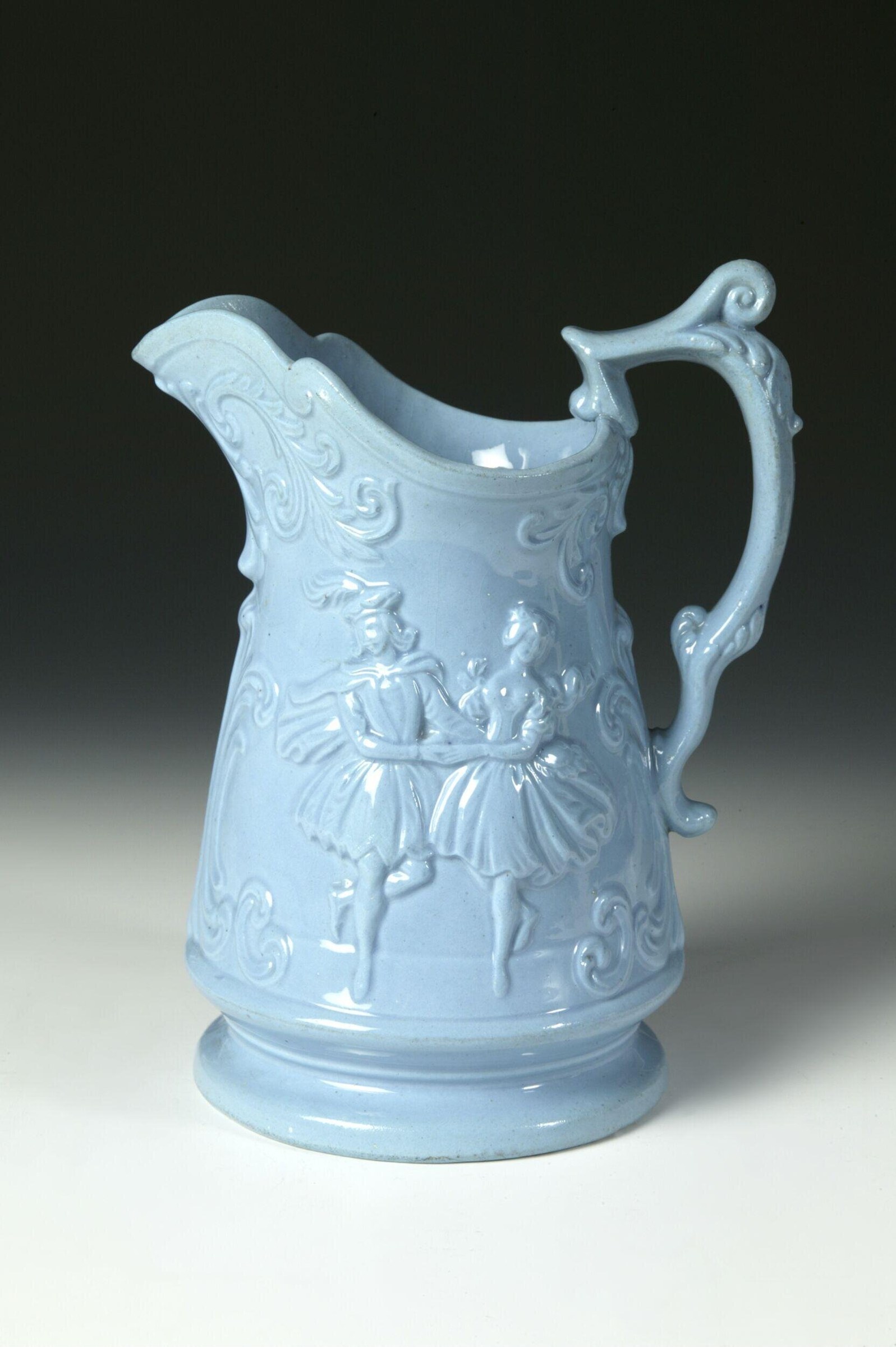 Pale blue ceramic jug with white relief ornament showing two classical figures in Regency dress within scrollwork frame.
