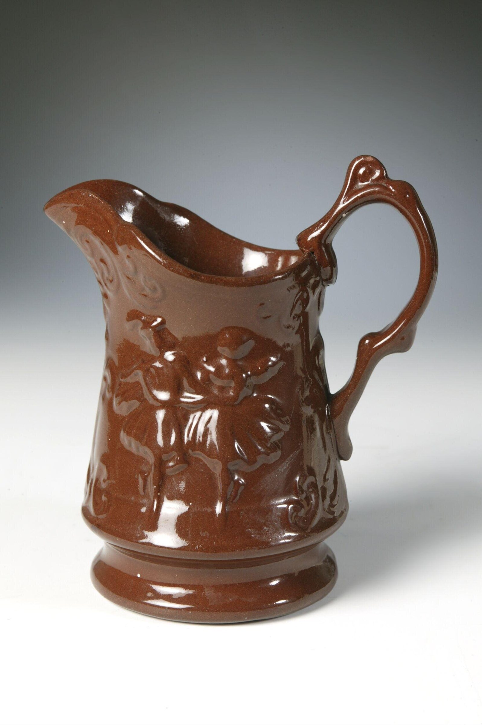 Reddish-brown ceramic pitcher with classical figures in relief, central figure in vigorous pose surrounded by attendants.