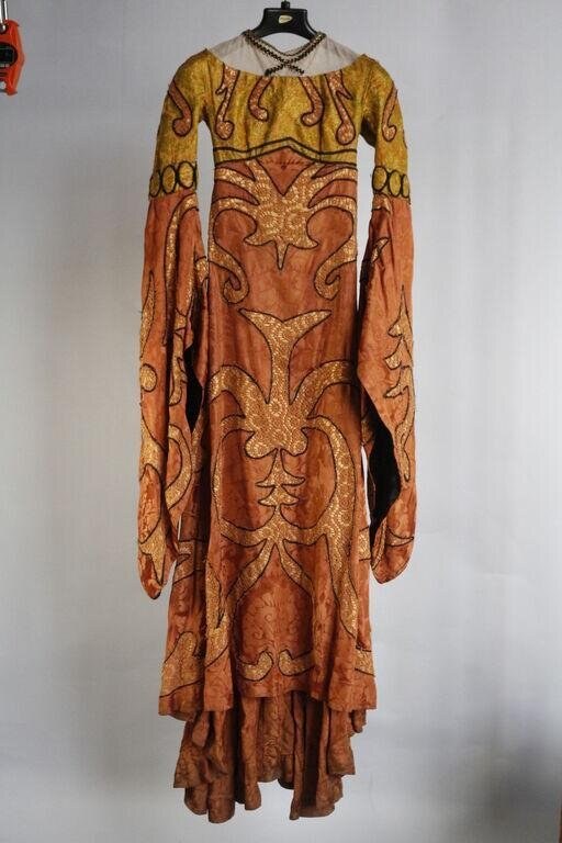 A full-length theatrical costume in golden yellow and terracotta orange with intricate gold embroidered ornament throughout, displayed on a mannequin.