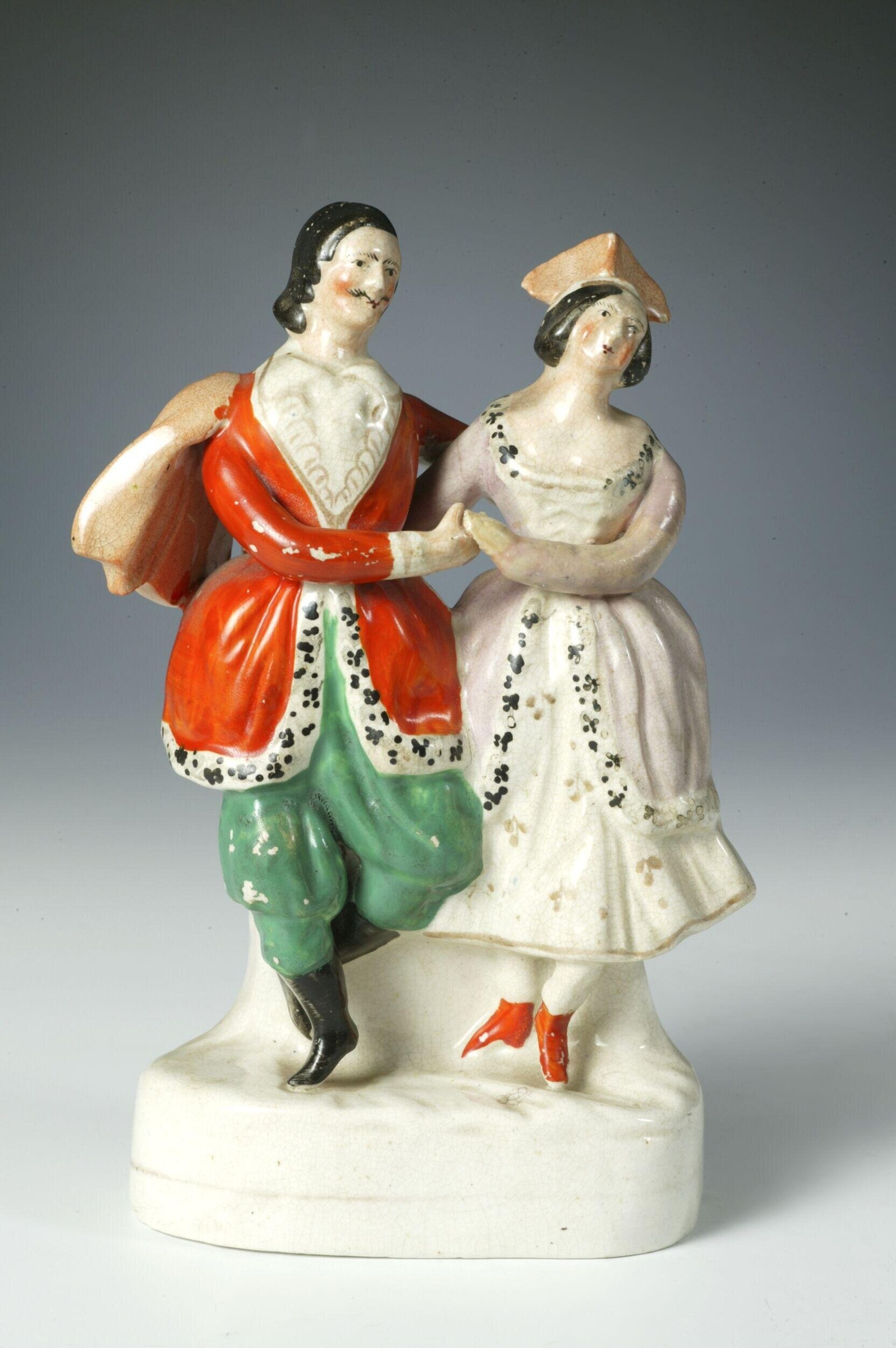 Porcelain figurine of two dancers in 1840s theatrical dress, hands joined, gazing upward in a formal partnered pose.