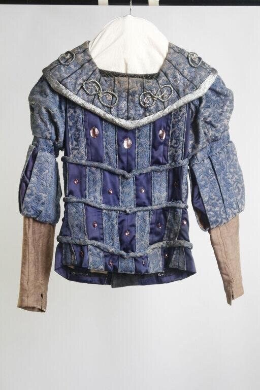 Blue-grey tailored jacket with elaborate metallic embellishment in geometric spiral and circle patterns, broad structured collar, navy panels with studs