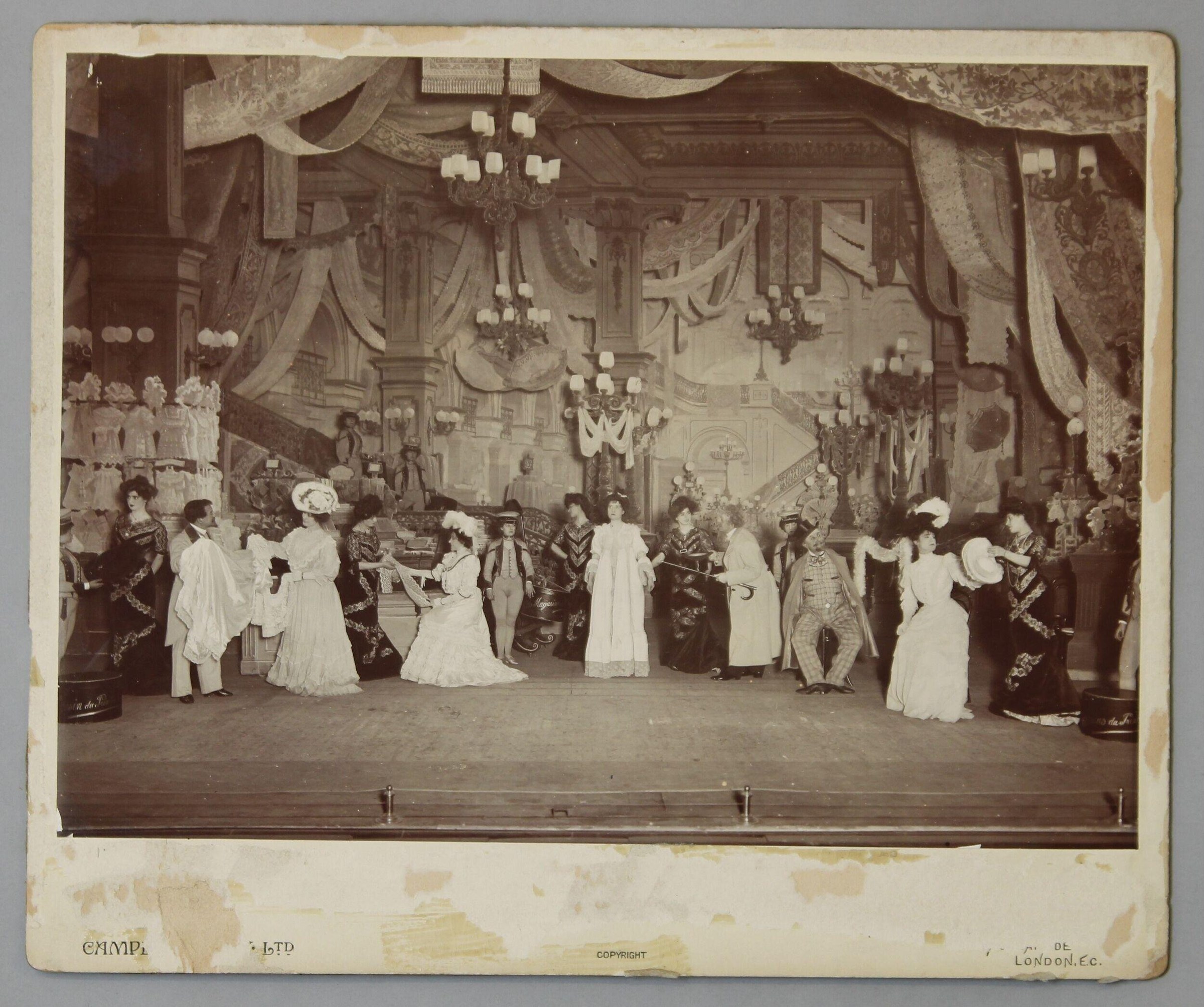 Sepia photograph of an ornate neoclassical ballroom set filled with figures in Edwardian evening dress, including women in white gowns and men in military