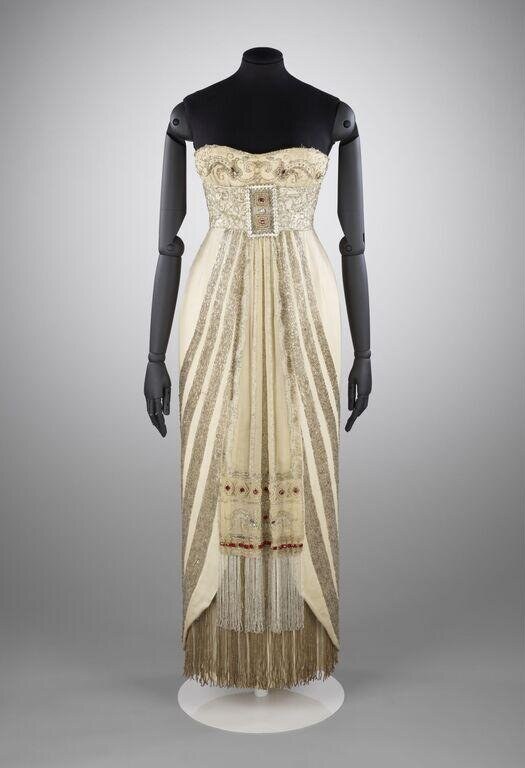 Ivory silk evening gown with beaded bodice and deep pleated skirt fringed at the hem, displayed on a dress form.
