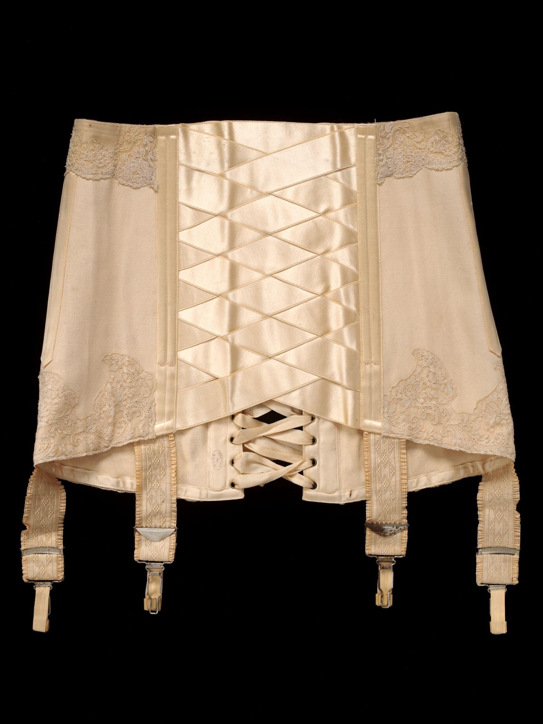 Cream silk corset with lace panels and elaborate front lacing, displayed flat with four garter tabs extending from the base.