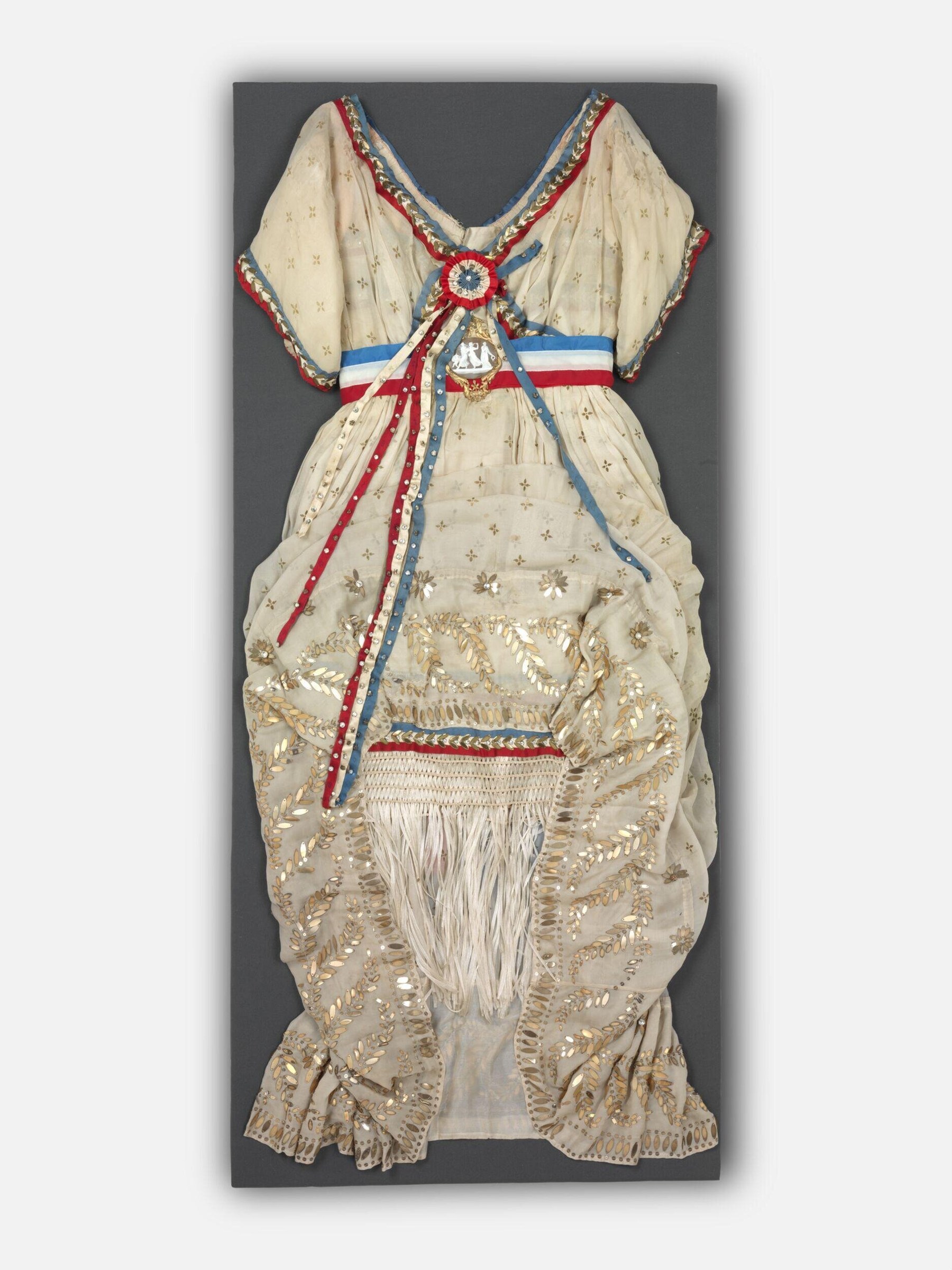 Cream silk theatrical costume with gold embroidery, tricolor ribbon at waist, and voluminous gathered skirt with deep flounces, circa 1912.