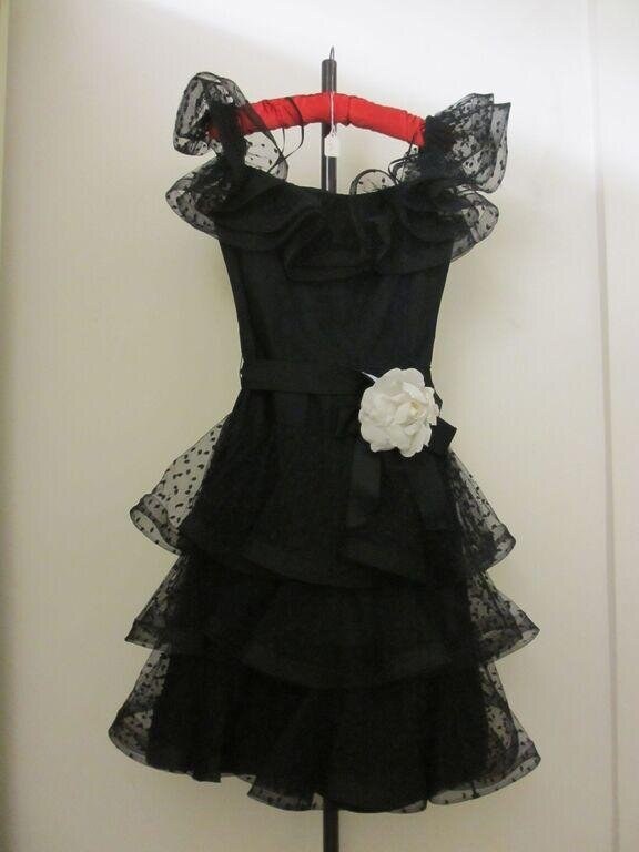 Black evening dress with tiered lace skirt, fitted bodice, and white flower detail, displayed on a dress form.