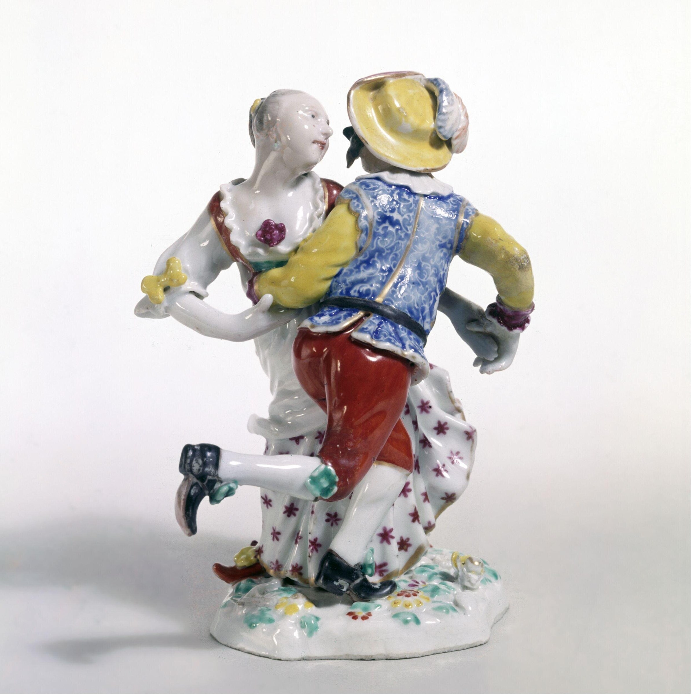 Porcelain figure group of two dancers, the man in yellow lifting a woman in white, both in 18th-century dress, on a flowered base.
