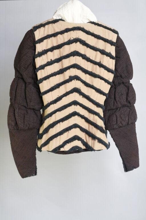 Quilted jacket with broad shoulders and voluminous sleeves, cream lining with dark chevron-striped back panel, displayed on a dress form.
