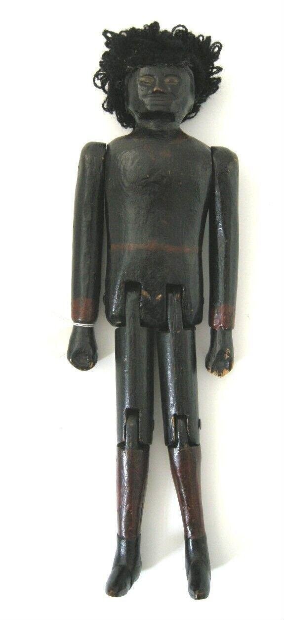 Dark wooden doll with elaborate coiled ringlets, static frontal pose, arms at sides, wrists and ankles banded with lighter material.