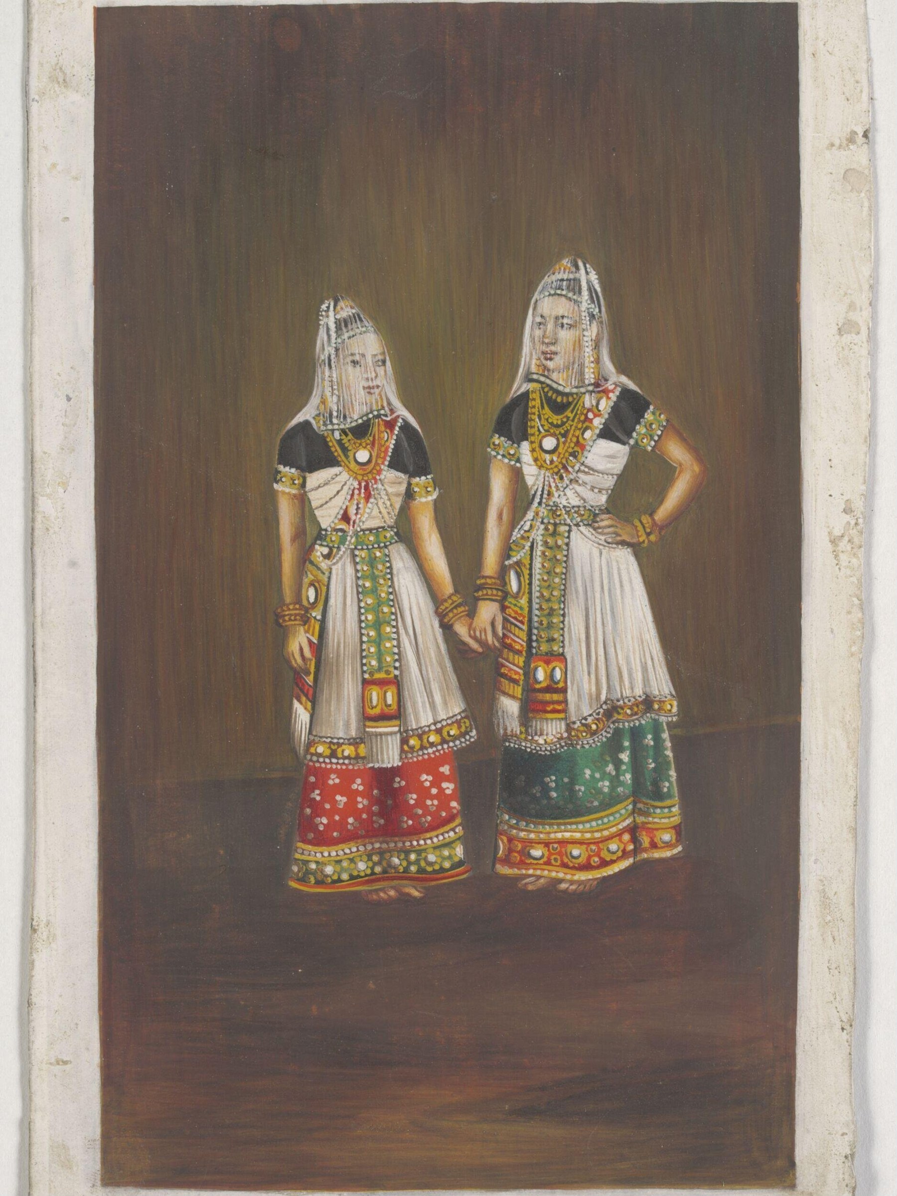Two young women in Manipuri classical dance costumes stand side by side holding hands, wearing pleated skirts, embroidered blouses, and tall conical